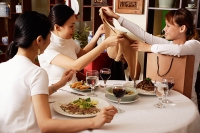 Women in restaurant, one woman showing clothing item to the others - Asia Images Group