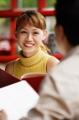 Woman holding menu, smiling, person in front of her, over the shoulder view - Asia Images Group