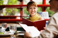 Couple in cafe, holding menus, woman smiling - Asia Images Group