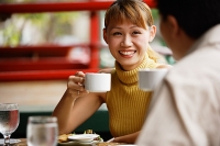 Couple in cafe, holding cups, woman smiling - Asia Images Group