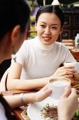 Women holding cups of coffee, sitting in cafe - Asia Images Group