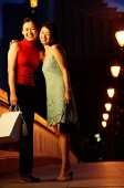 Two women standing, arms around each other, smiling at camera - Asia Images Group