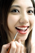 Woman smiling at camera, putting on lipstick with lip brush - Asia Images Group