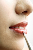 Close up of woman's mouth, putting on lipstick with lip brush - Asia Images Group