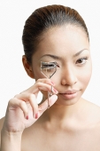 Young woman holding eyelash curler, looking at camera - Asia Images Group