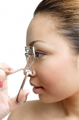 Young woman holding eyelash curler near eye, profile - Asia Images Group