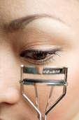 Young woman holding eyelash curler near eye, close up - Asia Images Group