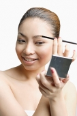 Young woman using eyebrow brush, looking at compact - Asia Images Group