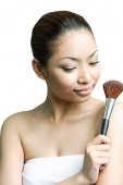 Woman holding make-up brush, looking away - Asia Images Group