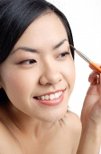 Woman holding brush, applying eyeshadow, looking away - Asia Images Group
