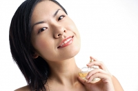Woman holding perfume bottle, looking at camera - Asia Images Group
