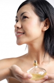 Woman holding perfume bottle, looking away - Asia Images Group