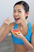 Woman eating grapefruit, looking at camera - Asia Images Group