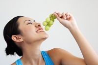 Woman holding grapes near mouth, side view - Asia Images Group