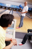 Man holding bowling ball, standing in bowling ally, turning to look at people behind him - Asia Images Group