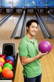 Man in bowling alley, holding bowling ball, looking at camera - Asia Images Group