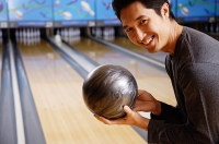Man holding bowling ball, smiling at camera - Asia Images Group
