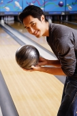 Man bending, holding bowling ball, smiling at camera - Asia Images Group