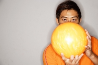 Man holding bowling ball in front of face - Asia Images Group