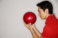 Man holding bowling ball in front of face, side view - Asia Images Group