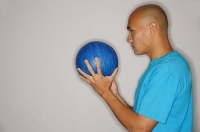 Man holding bowling ball in front of face, looking away - Asia Images Group