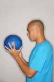 Man holding bowling ball looking away - Asia Images Group