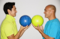 Two men standing face to face, carrying bowling balls, smiling - Asia Images Group