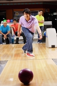 Man bowling, friends watching in the background - Asia Images Group