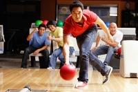 Man bowling, friends cheering in the background - Asia Images Group