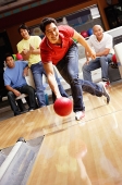 Man bowling, friends cheering in the background - Asia Images Group