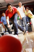 Man bowling, friends in the background, cheering - Asia Images Group