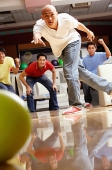 Man bowling, friends in the background, cheering - Asia Images Group