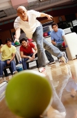 Man bowling, friends in the background, watching - Asia Images Group