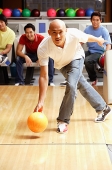 Man aiming bowling bowl, friends in the background, watching - Asia Images Group