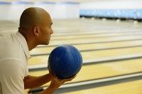 Man holding bowling ball, preparing to bowl - Asia Images Group
