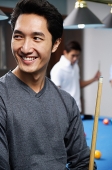 Man holding pool cue, smiling, looking away - Asia Images Group