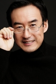 Man adjusting glasses, smiling, black background - Asia Images Group