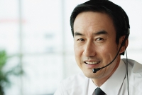 Businessman looking at camera, wearing headset - Asia Images Group