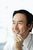 Businessman using headset, smiling, looking away - Asia Images Group