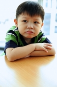 Young boy looking away, arms crossed, leaning on table - Asia Images Group