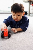 Young boy lying on floor, playing with toy tractor - Asia Images Group