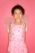 Young girl in pink dress with wings attached, looking at camera - Asia Images Group