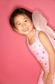 Young girl in pink dress with artificial wings, smiling at camera - Asia Images Group