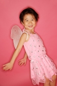 Young girl in pink dress with artificial wings, smiling at camera, hands stretched behind her - Asia Images Group