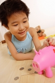 Young girl lying on floor, putting money in piggy bank - Asia Images Group