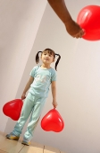 Girl holding balloon, looking at someone standing in front of her - Asia Images Group
