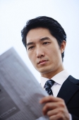 Businessman reading newspaper, serious expression - Asia Images Group