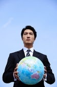 Businessman holding globe with both hands, looking away - Asia Images Group