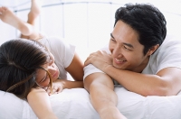 Couple side by side on bed, looking at each other - Asia Images Group