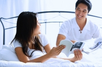 Couple on bed, woman turning to show man book - Asia Images Group